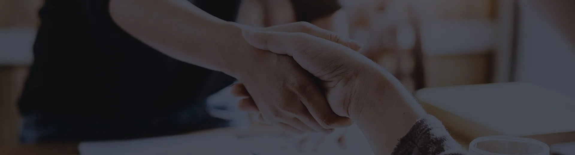 Two people shaking hands across a table after reaching an agreement