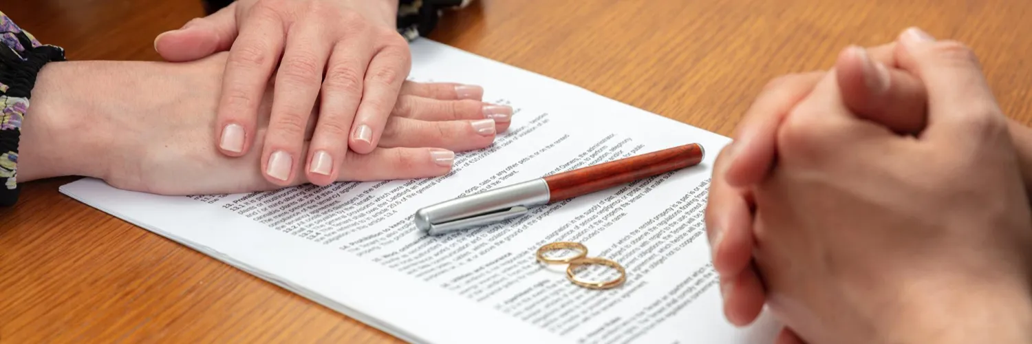Couple's hands resting on divorce papers beside a pen and two wedding rings
