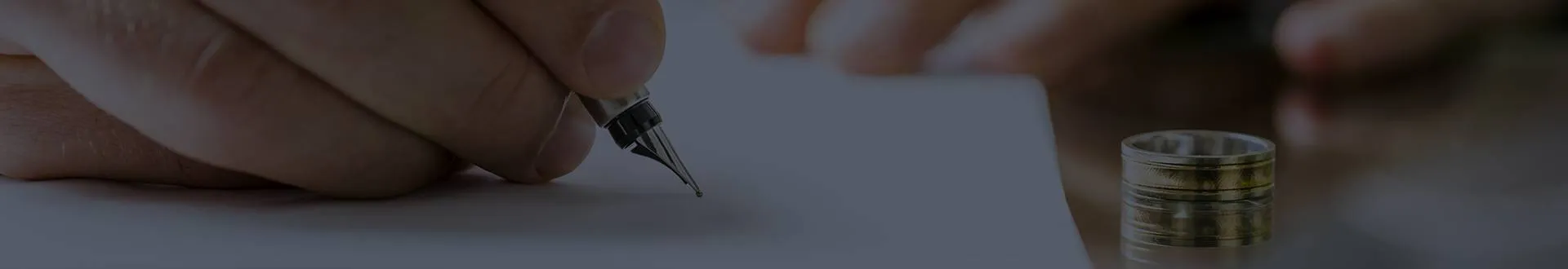 Hand signing divorce papers with a fountain pen beside a wedding ring