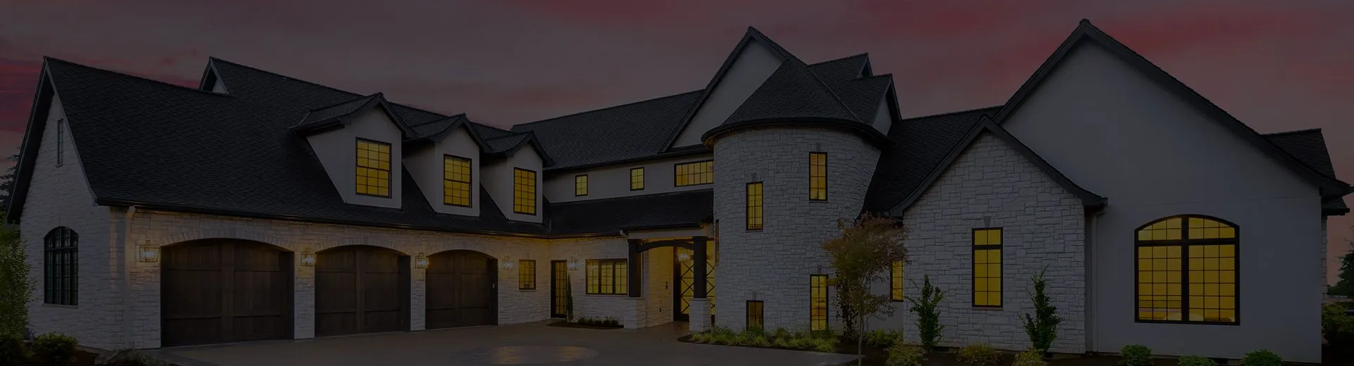 Large stone family home with a three car garage at dusk